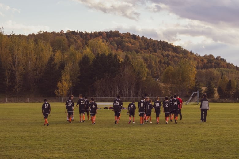 A group of soccer players, seen from behind, walking across a field