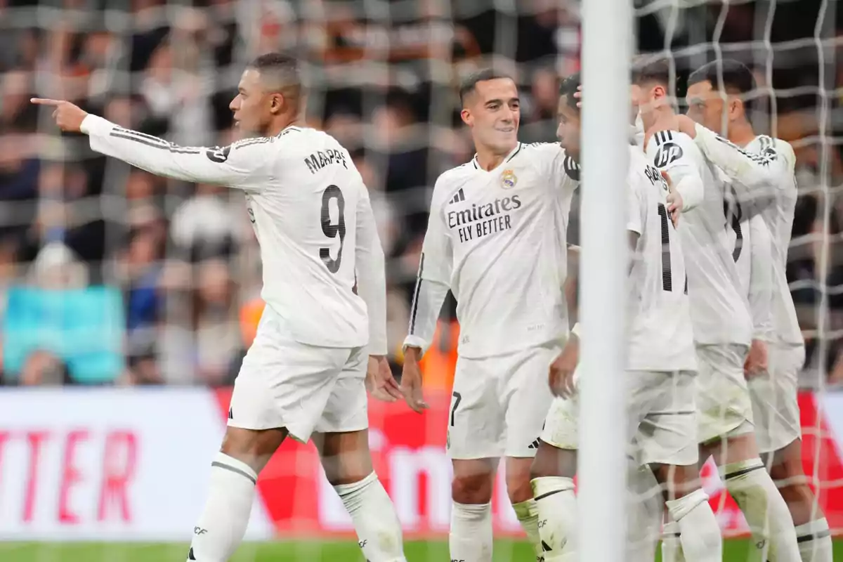 Football players in white uniforms celebrate on the field during a match.