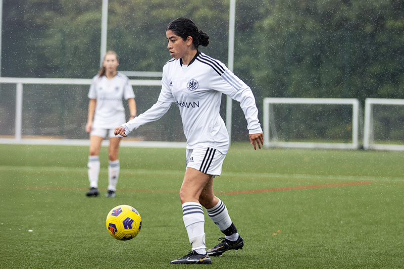 A young woman on an outdoor field gets ready to pass a soccer ball.